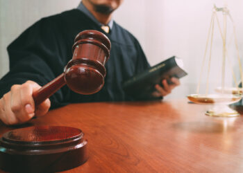 justice and law concept.Male judge in a courtroom with the gavel and working with holy book and brass scale on wood table